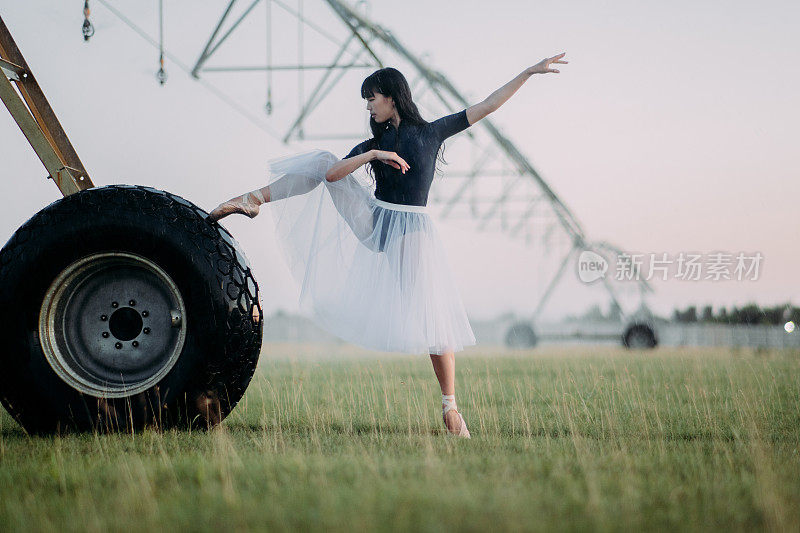 一名芭蕾舞演员在农场里靠近农业喷雾器的轮子跳舞。