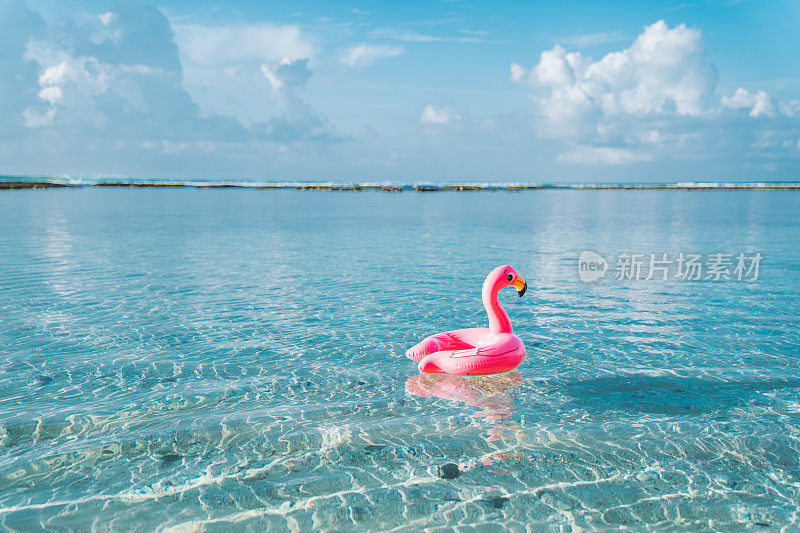 充气粉红色火烈鸟漂浮在透明的绿松石海。蓝色的天空，很少有云的背景。