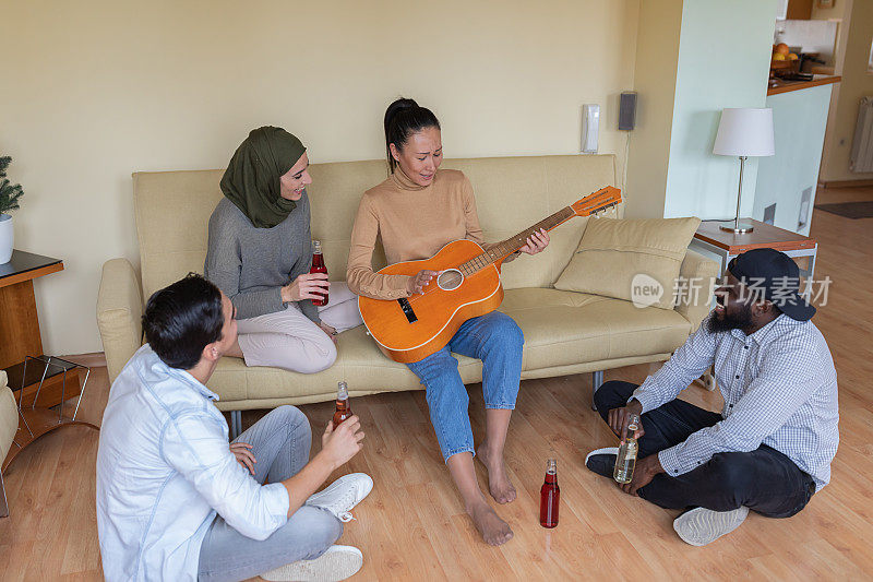 一群年轻的多元文化朋友正在享受吉他的声音和清爽的饮料。