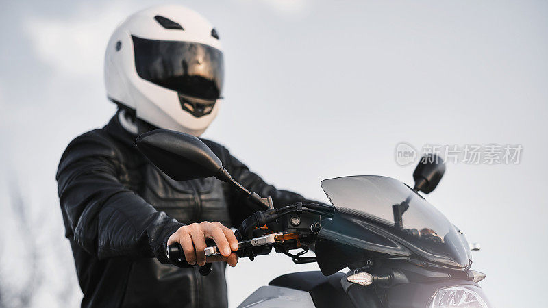 一个年轻人的肖像，坐在摩托车上，穿着皮夹克和头盔。