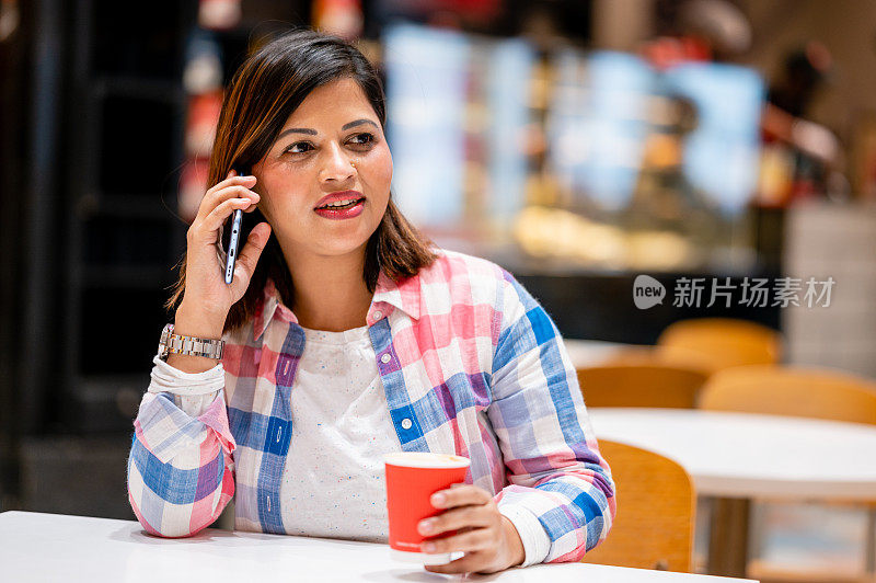 年轻女子坐在咖啡馆边喝咖啡边玩智能手机。