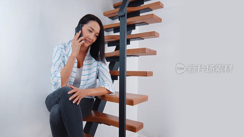 一个女人坐在楼梯上，一边发短信一边打电话