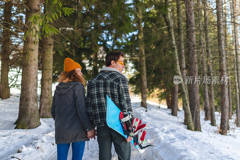 一对年轻的异性恋情侣手牵着手走过雪原森林