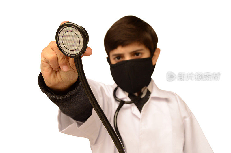 一个9岁的男孩穿着医生的衣服，戴着黑色的面具和白色的实验服，脖子上挂着听诊器，手里拿着听诊器，就像在白色的背景上检查，上面有文字的拷贝空间