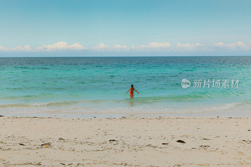 在桑给巴尔岛，一名女性游客在碧绿的海洋旁欣赏清晨美景