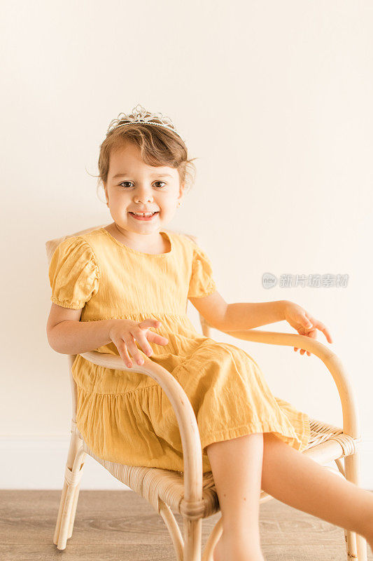 一个将近3岁的幼童，棕色卷发和棕色眼睛，穿着黄色的连衣裙和头饰