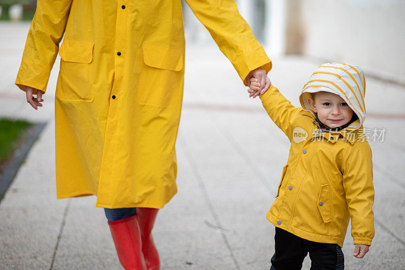 母亲和蹒跚学步的孩子，男孩，穿着雨靴和雨衣在雨中玩耍