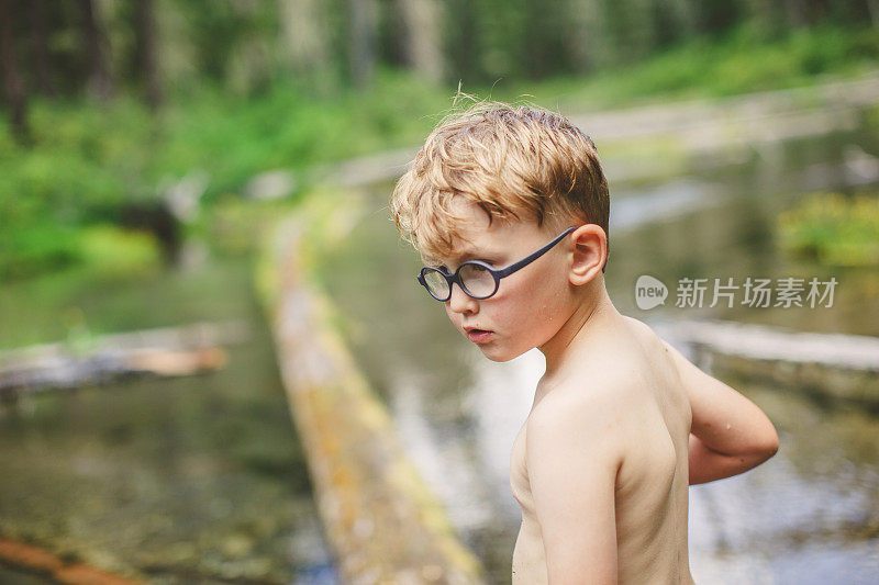 小男孩在森林溪流上的原木上保持平衡