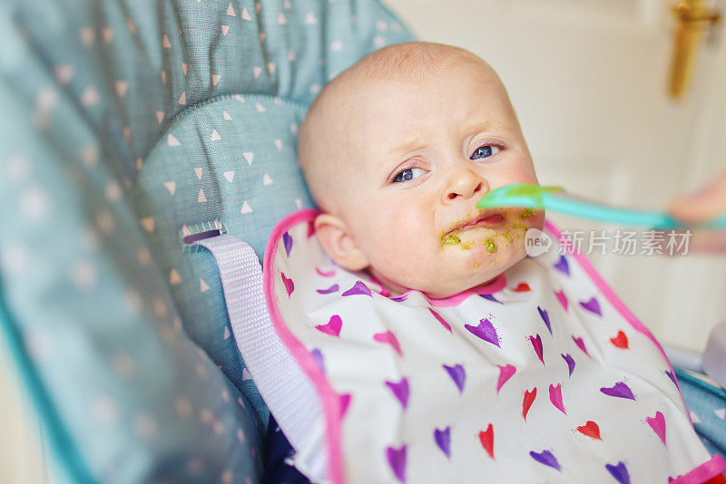 年轻的妈妈给她不太确定的女儿断奶，吃着花椰菜泥，当她第一次尝到花椰菜泥时，她的表情多种多样。
