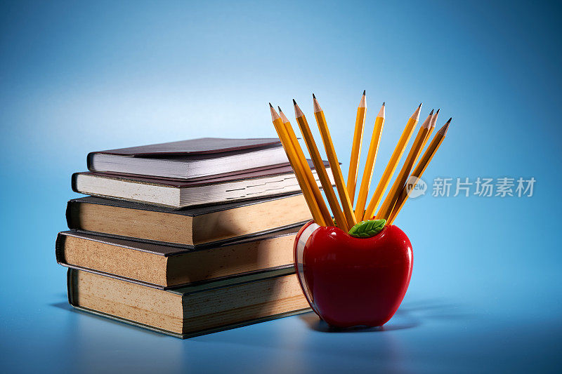 苹果形状的铅笔筒，蓝色的背景上有一摞书