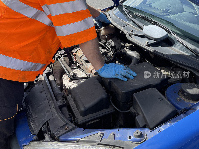 蓝色汽车在路边抛锚的全帧图像，打开的汽车引擎盖显示发动机正在由车辆故障协助修复，汽车机械师穿着反光的，高能见度的夹克