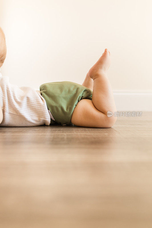 2022年，患有多指畸形的7个月大的大流行男婴，穿着橄榄绿颜色的可重复使用和可持续的布尿布，在家里的木地板上爬行，以下犬式和腹部躺着