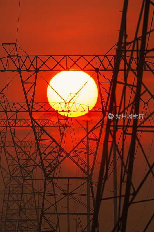 炎炎夏日，太阳落在一排高压输电塔后面