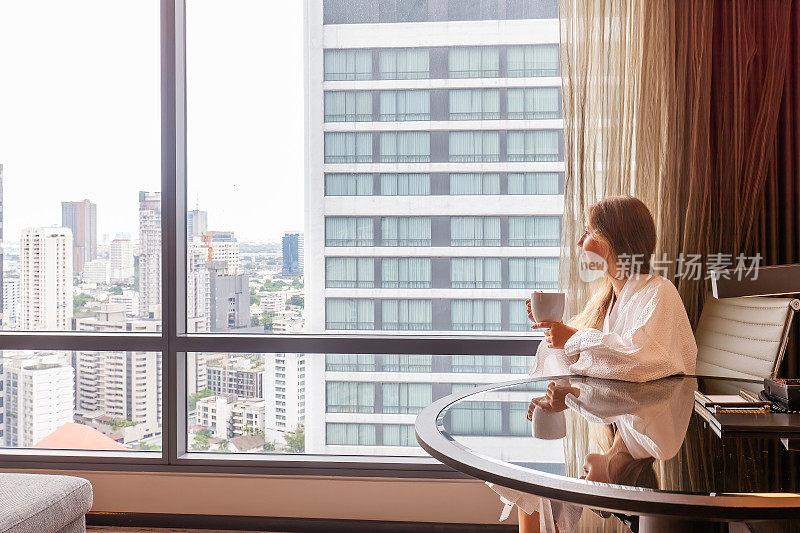女人穿着浴袍拿着咖啡杯坐在现代酒店或公寓