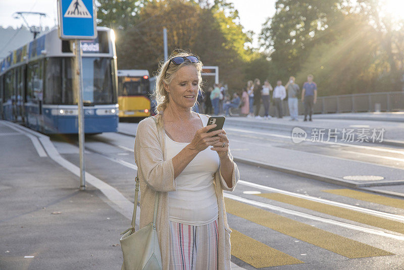 老妇人走在老城区的街道上，用着智能手机