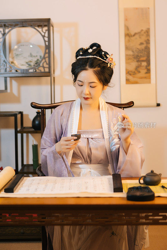 一位亚洲美女穿着汉服，在家喝茶，写书法