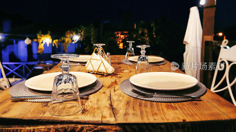 夏日傍晚，露台上的空桌子上装饰着玻璃杯、餐具、盘子和餐垫。供人用餐的装饰好的空桌子