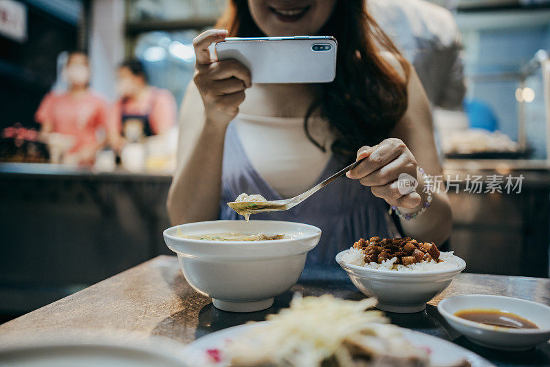 一名亚洲女子在旅游目的地观光，在品尝当地美食之前，她用智能手机捕捉了旅行的记忆。