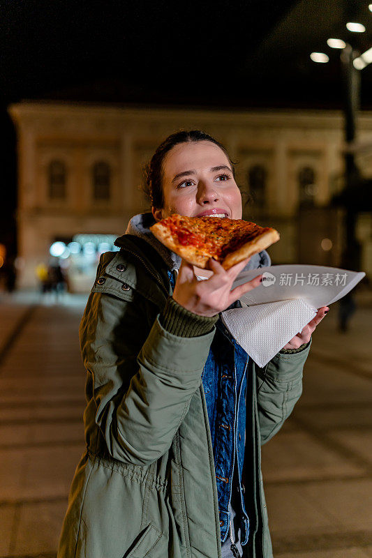 一位年轻女子在凉爽的夜晚吃了一片披萨