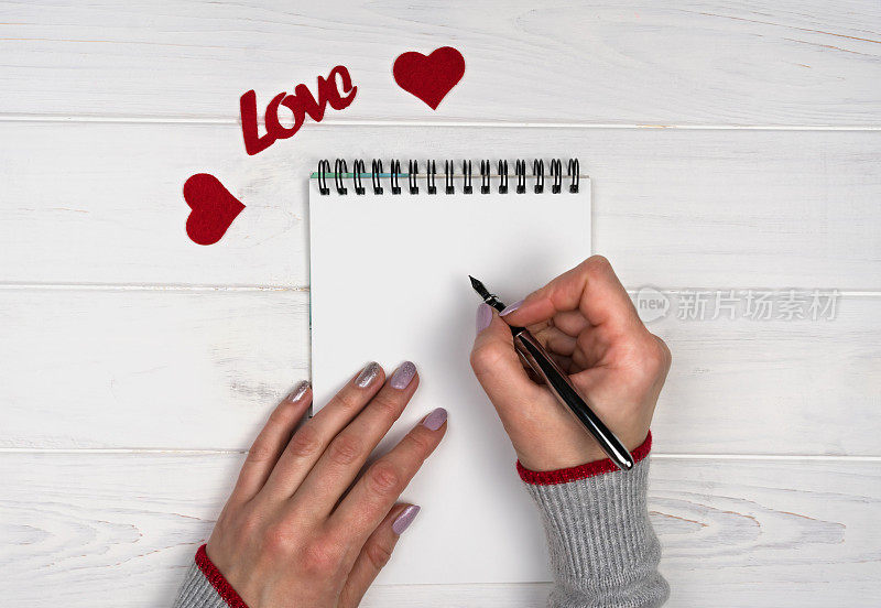 女人的手在记事本上写下爱的信息。Flatlay组成。情人节的情书。情人节假期概念。前视图。
