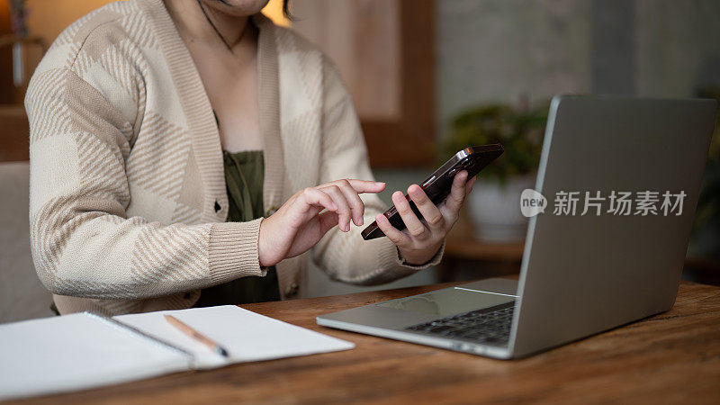 一名亚洲女性在咖啡店远程工作时使用智能手机的剪辑图片。