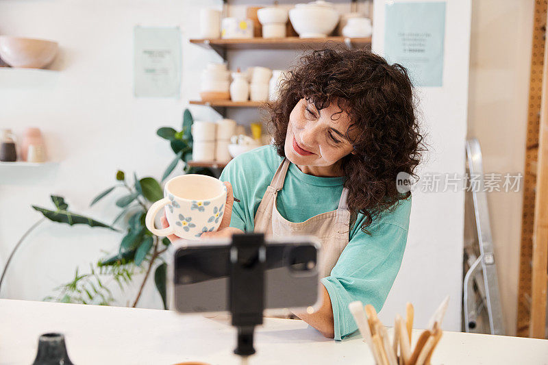 一名女视频博主在陶器作坊里画着一杯粘土