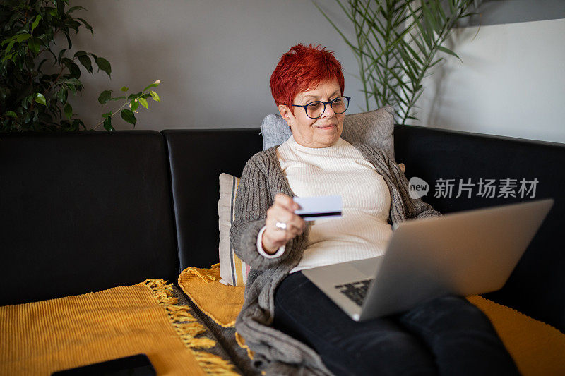 一位面带微笑的老年妇女坐在客厅里，用笔记本电脑在网上购物。