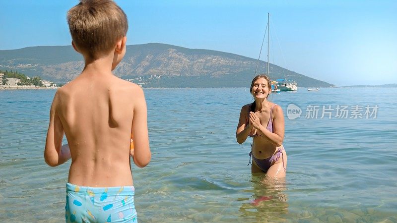 一个快乐的女人和她的儿子在海边玩飞盘，玩得很开心。家庭假期，孩子和父母的假期和有趣的夏日时光。