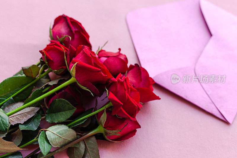 照片上有两朵玫瑰，桌子上有一个粉红色的信封