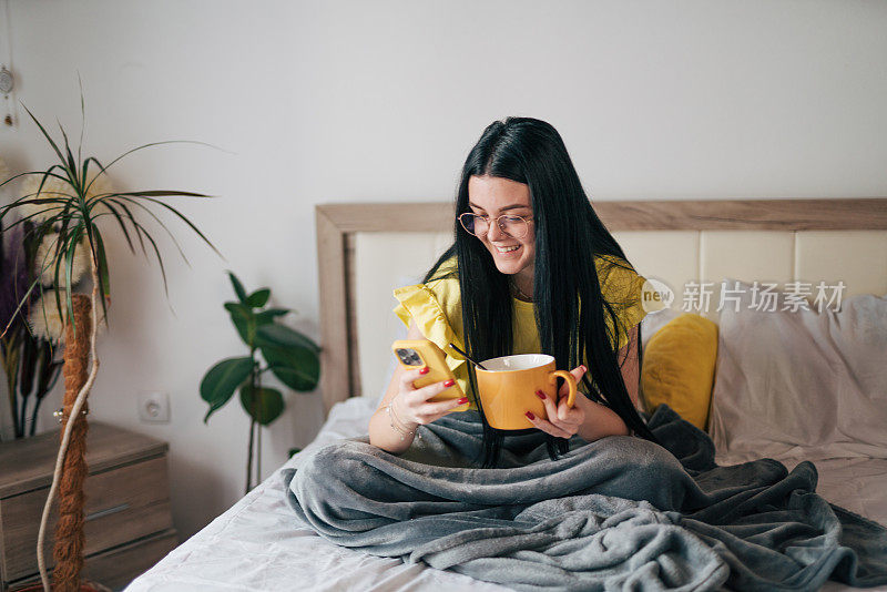 一个年轻的女人正在床上吃早餐，用她的智能手机。