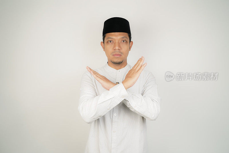 亚洲穆斯林男子表现出“停止”或“拒绝”的表情，双臂交叉做否定的手势，孤立的背景。