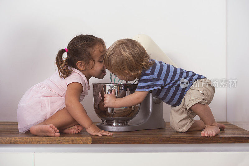 两个可爱的孩子直接舔着搅拌器里的鲜奶油。
