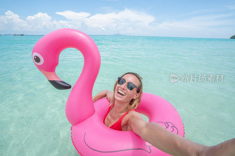 一个年轻的女人在恬静的海滩上与粉红色的火烈鸟在清澈的海水中自拍在泰国群岛。人们旅行奢侈，乐趣和酷的态度概念