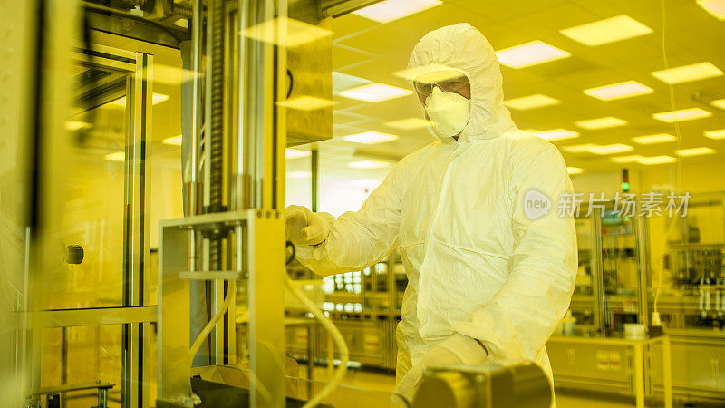 在制造设施拍摄的科学家在无菌防护服在工业3D打印机器上工作。生物技术的制造过程。用黄色滤光片从内部拍摄。