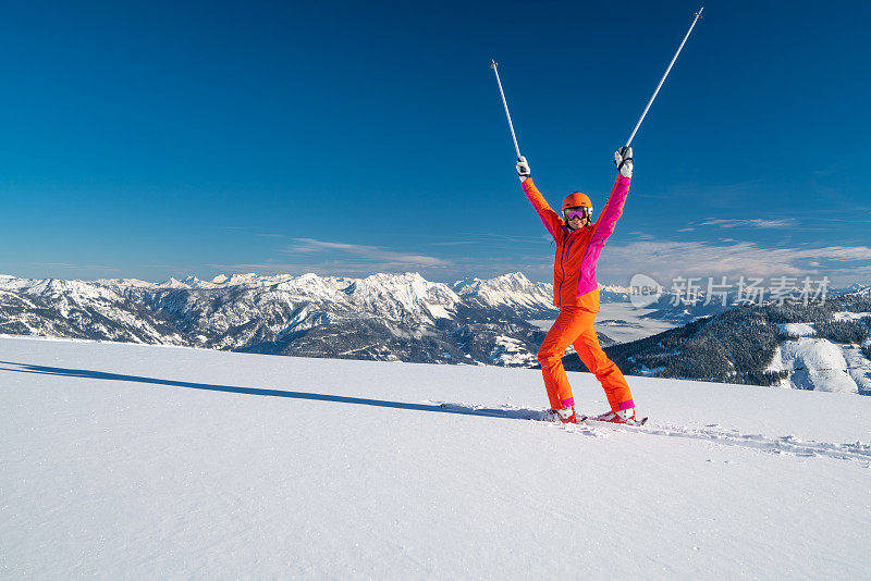 快乐的滑雪女子站在深雪在阳光明媚的冬日晴朗的蓝天山全景
