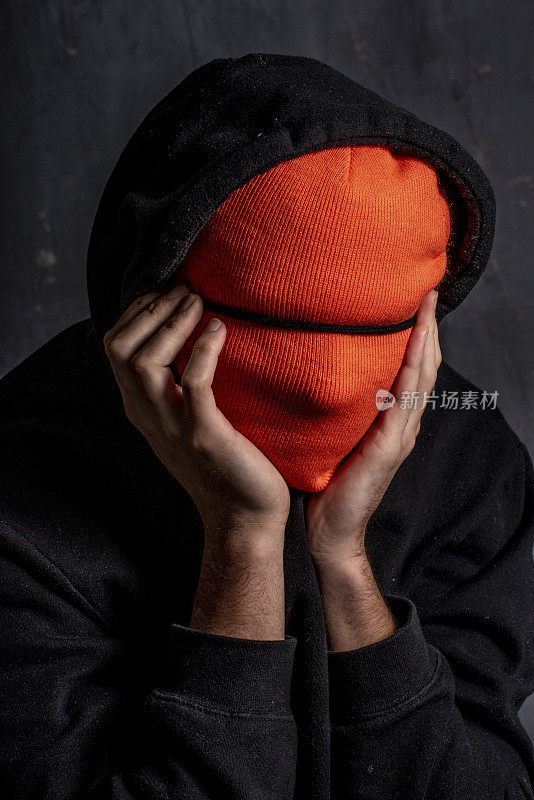 一名少年用一顶橙色的无檐帽遮住脸来表达自己的情绪。
