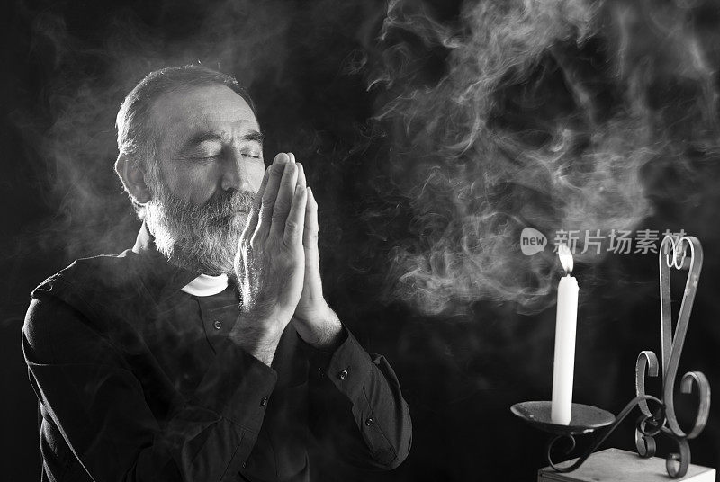 在烛光下在黑暗中祈祷的资深牧师