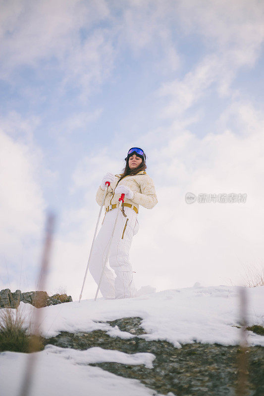 近景美丽的年轻女子在冬天的衣服站在一边，手拿木棍的背景雪山