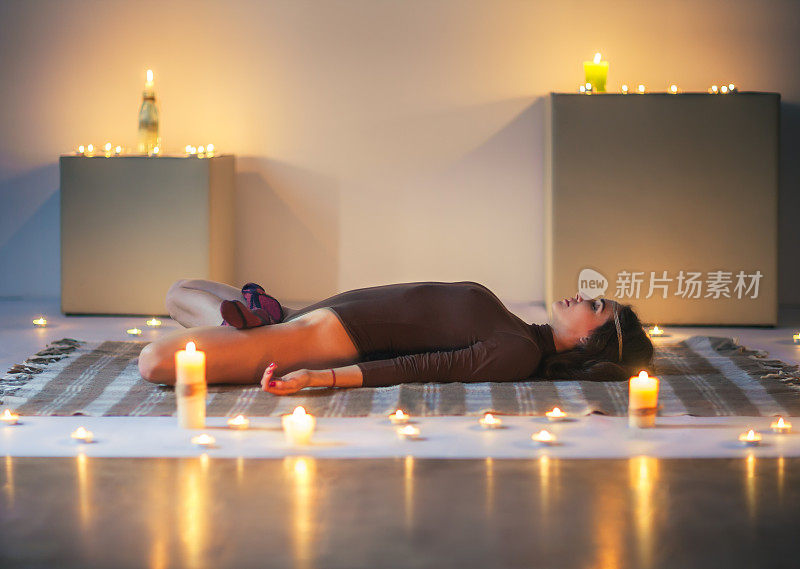 年轻美丽的女人做瑜伽体式睡仰卧荷花在格子在舒适的房间蜡烛