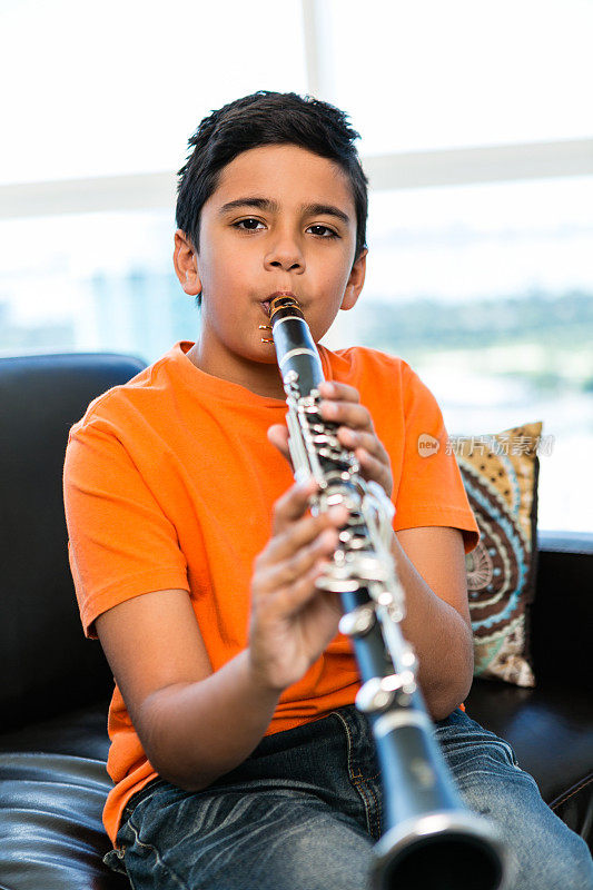 可爱的男孩在家里吹单簧管的肖像