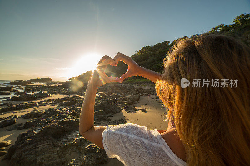 年轻女子把海滩上的夕阳画成心形