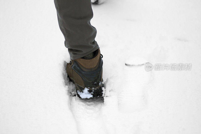 男人的腿在徒步靴，行走在雪中(特写)