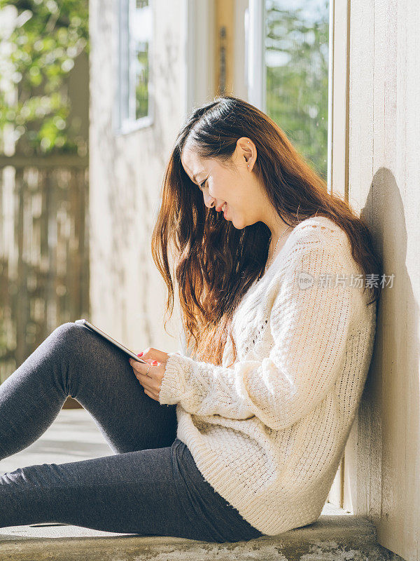 亚洲妇女坐在阳台上拿着平板电脑