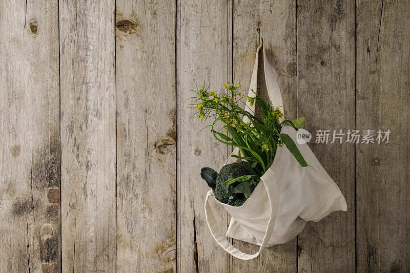 绿叶蔬菜装在一个天然棉花可重复使用的袋子里，挂在一个旧的风化的木板墙上。
