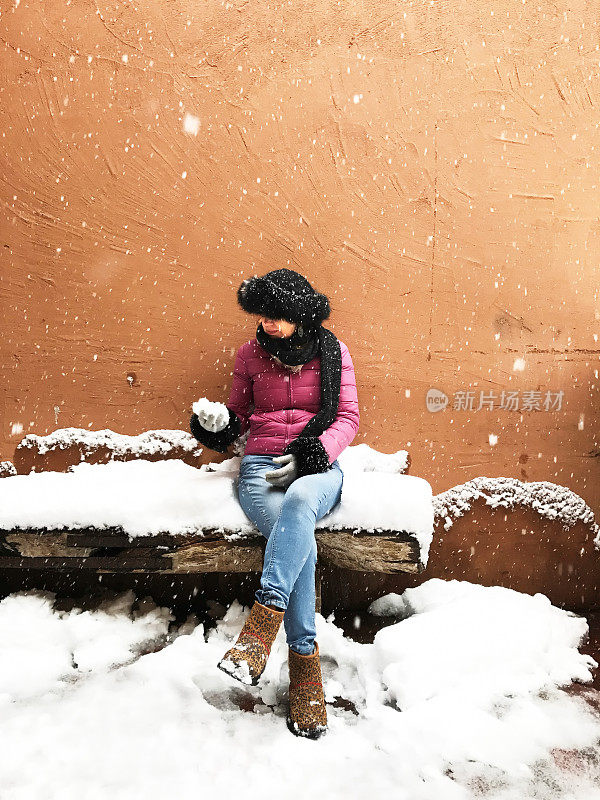下雪:女人和雪球坐在下雪的长凳上