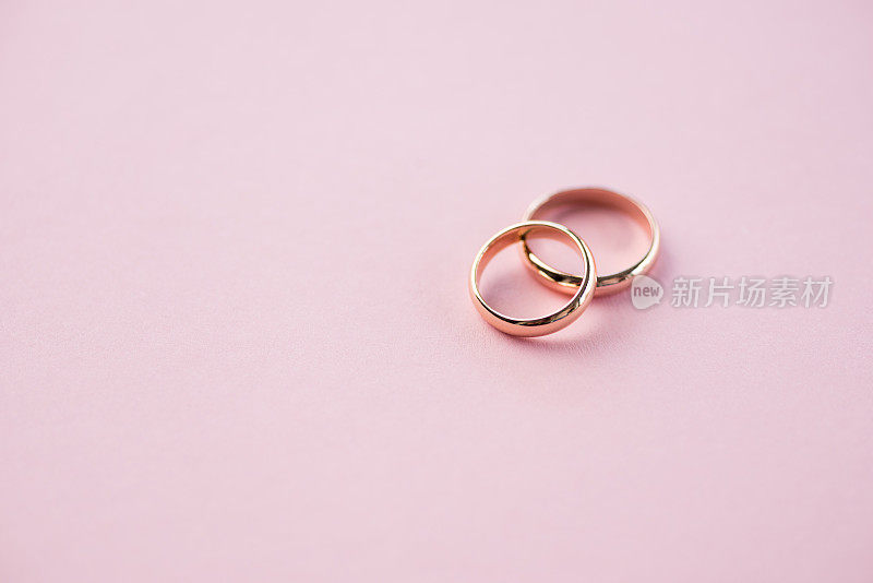 近景闪亮的金色结婚戒指上的粉红色，结婚戒指的背景