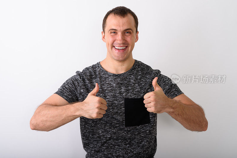 工作室拍摄了一个年轻的快乐的肌肉男，在白色的背景下竖起大拇指微笑着
