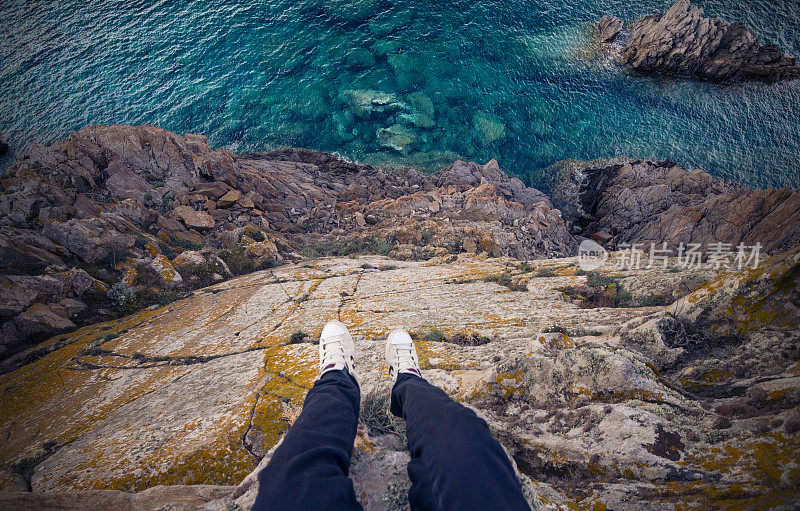 一个男人站在意大利海岸的悬崖上，下面是地中海。波尔图切尔沃-翡翠海岸，撒丁岛-意大利