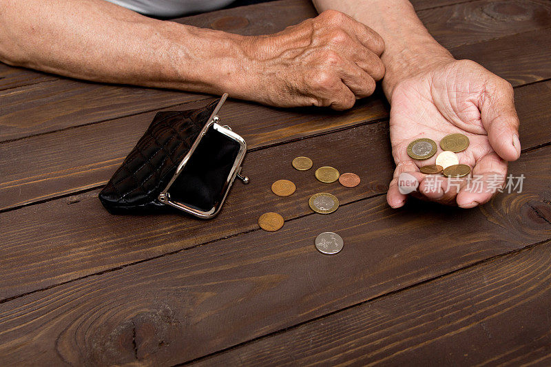 一个老人把硬币放在空空的旧皮夹上。退休后贫困的概念。