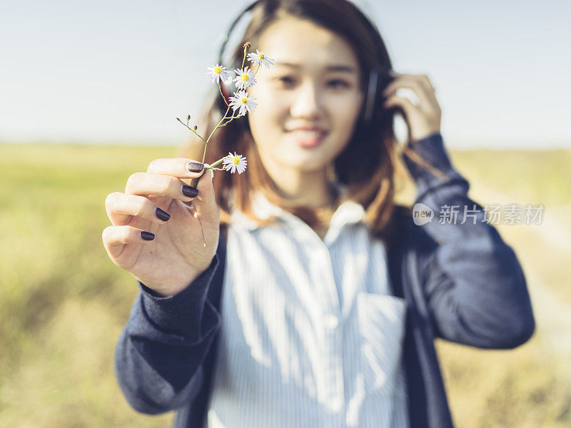 年轻的女孩戴着耳机在野外，手持鲜花